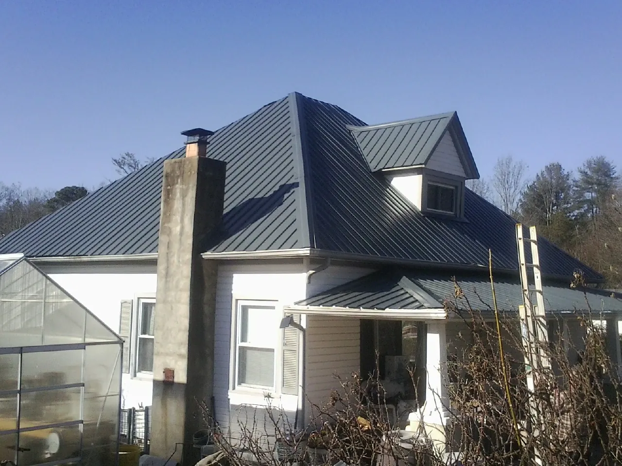 Dark blue standing seam metal roof on a white farmhouse with dormer — Slate & Tile Roof Repair by Roofing Brothers in Ashford