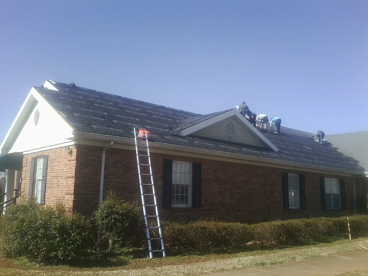 Crew tearing shingles off a brick ranch roof with a ladder set — Emergency Roof Repair work by our crew in Ashford